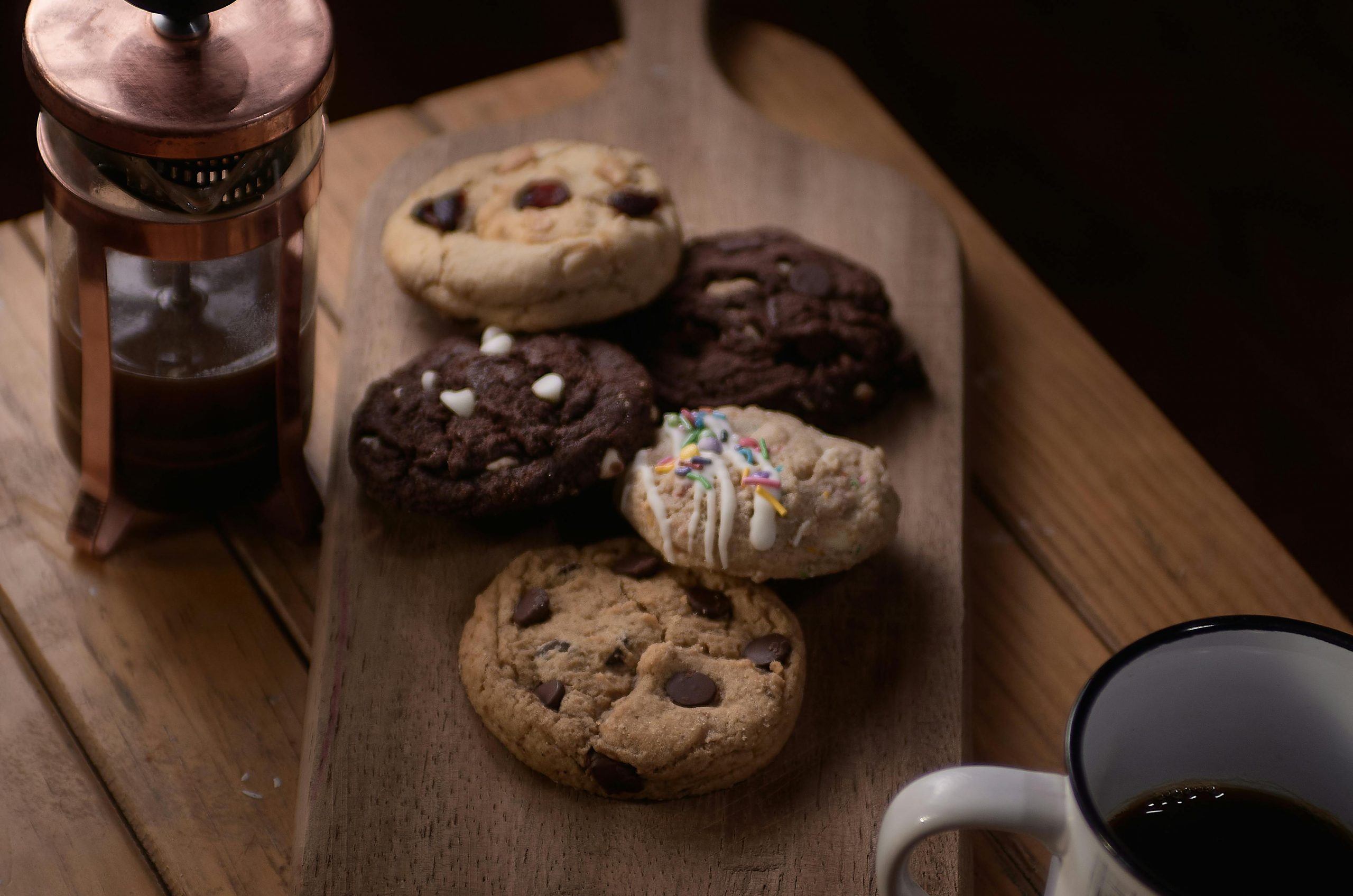 A rustic display of assorted cookies on a wooden board, paired with coffee.